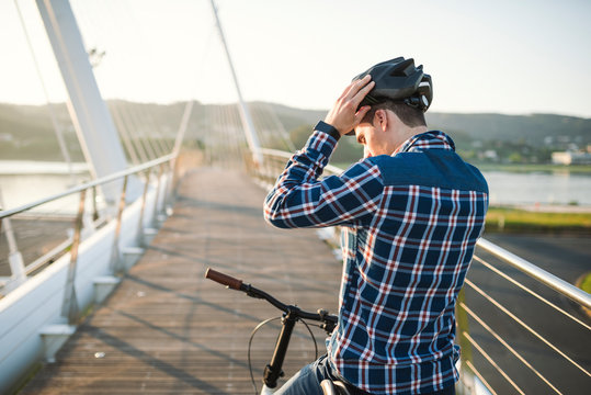 Young man on bicycle putting on helmet on a bridge