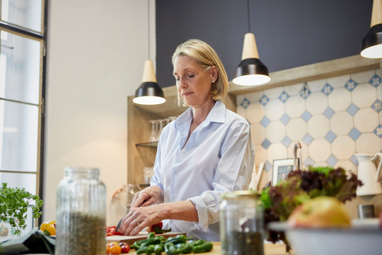Mature woman chopping bell pepper in kitchen
