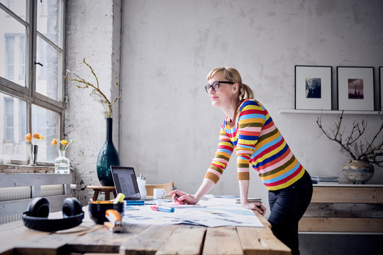 Portrait of smiling woman standing at desk in a loft looking through window