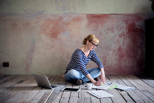 Woman sitting on wooden floor in an unrenovated room of a loft working