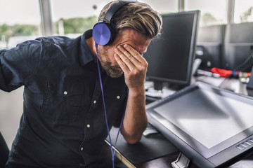 Tired graphic designer using digital tablet, wearing headphones