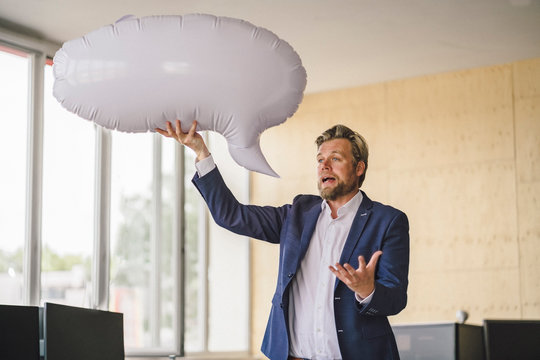 Businessman standing in office, holding inflatable speech bubble