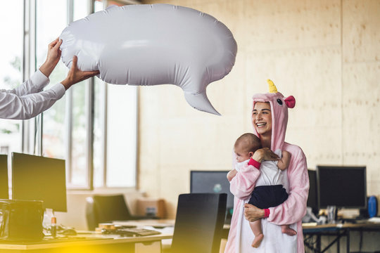 Young mother in unicorn onesie, holding her son in her arms, with speech bubble over her head