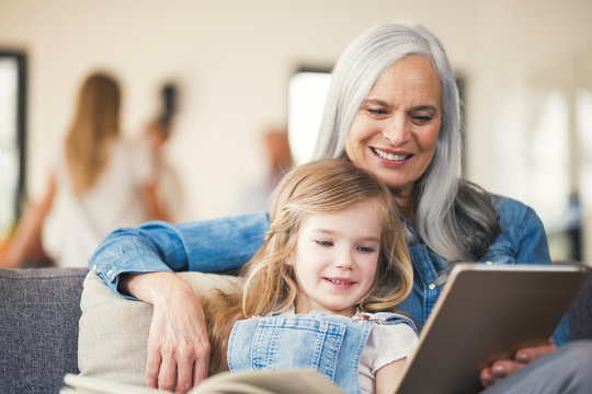 Grandmother and granddaughter sitting on couch, reading together