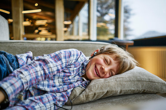 Happy boy lying on couch with earphones