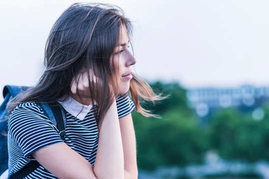 Pensive young woman with backpack leaning on railing