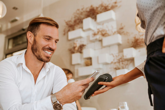 Smiling man paying with smart phone in cafe