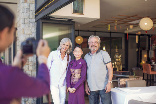 Senior couple taking pictures with Asian waitress in front of restaurant