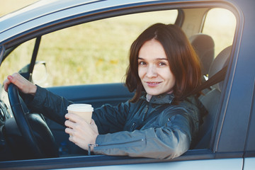 Naklejka premium pretty young smiling woman driver holding paper coffee cup