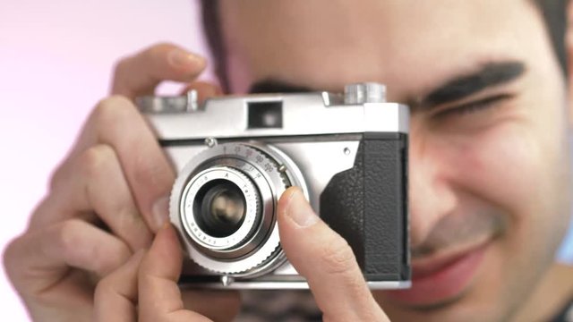 Young man using an old vintage film camera to take pictures. Closeup on his head and camera resting against the viewfinder focusing on the scene.