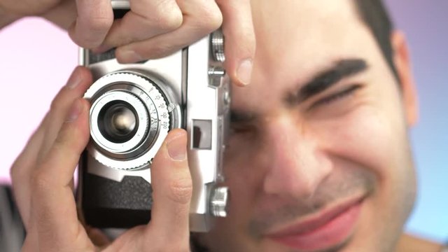 Young man using an old vintage film camera to take pictures. Closeup on his head and camera resting against the viewfinder focusing on the scene.