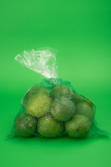 fresh limes or lemons in packaging bag on green background monochromatic green