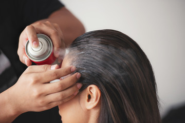 hairdresser fixing a coiffure with ringlets of a woman using a hair spray in a beauty salon