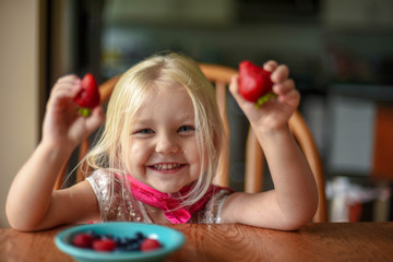 Fototapeta na wymiar Smiling little girl sitting at the kitchen table eating fresh berries