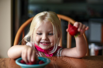 Happy little girl in the kitchen eating fresh berries