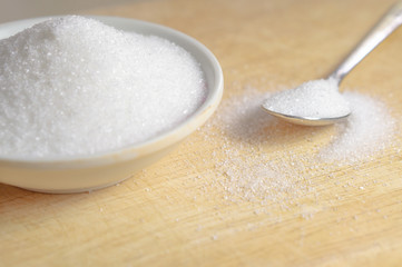 Fototapeta na wymiar Sugar in a white cup with a spoon with white sugar placed on the side of a cup on a wooden floor.