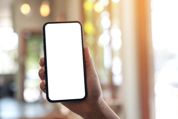 Mockup image of a hand holding and showing black mobile phone with blank white screen in modern cafe