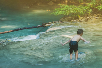 Little boy crossing a river full of stones carefully and teetering in waterfall at Erawan National Park in Kanvhanaburi,Thailand.