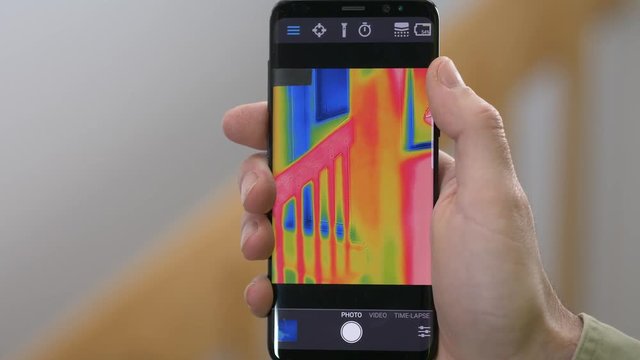 Worker inspecting using a thermal imaging camera connected to a smartphone. Trying to find water leaks, heat loss and take the temperature of objects. Thermography concept.