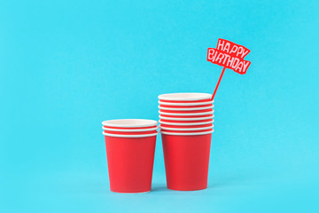 Colorful red paper cups and happy birthday spike party on blue background with copy space
