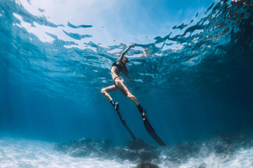 Woman freediver with fins swim over sandy sea and sun rays underwater