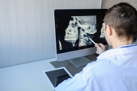 back view of a male radiologist examining neck x-rays (cervical vertebrae) on computer