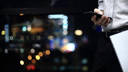 business man prepare for big meeting. man carrying computer notebook and checking on smartphone. businessman in a modern office with bokeh defocus lights from city outside of the window.