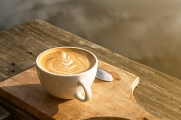 Cup of latte coffee with art milk foam on wooden chopping board at morning.