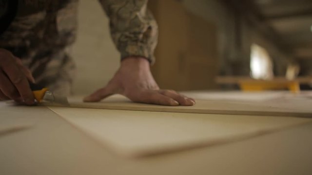 A man cuts veneer pieces for further furniture assembly, close-up, process