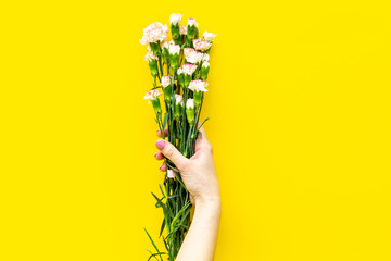 Bouquet of pink carnation in female hands on yellow background top view space for text