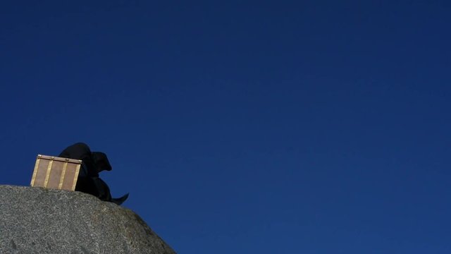 man in hoodie near chest with jewels praying at egde of cliff slow motion - philosophy about wealth