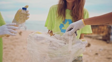 The volunteers raises and throws plastic garbage into the bag. Group of volunteers cleaning up beach. Volunteering and recycling concept. Environmental awareness concept copy space