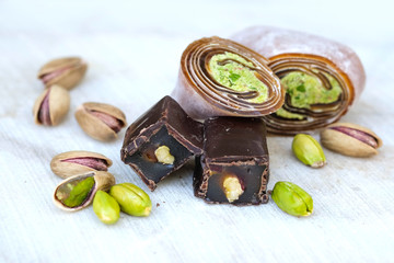 Eastern Turkish sweets with pistachios on a white wooden background. Chocolate candy with pistachios, baklava and pistachio nuts around.