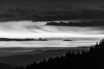 Trees silhouettes against the sky at dusk, with mountains layers in the background