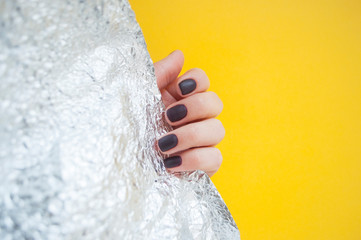 Young woman's hand with beautiful manicure on yellow background with metallic shiny paper.