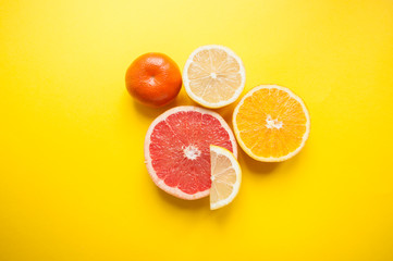 Flat lay of cut ripe juicy grapefruit, lemon and orange on yellow background. Citrus pattern.