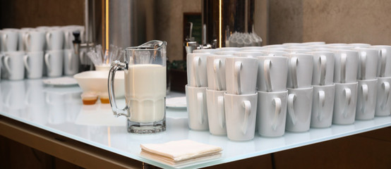 close-up of White cups and a jug of milk on a light table