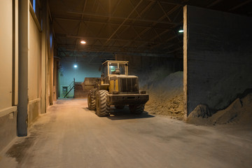 Fototapeta na wymiar Tractor moves the sand in the cement plant. Dark room with lights