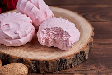 Three zephyrs with raspberries on a wooden stand next to nuts and various decorative elements on the dark wooden background. Close-up
