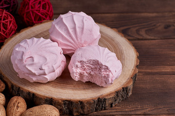 Three zephyrs with raspberries on a wooden stand next to nuts and various decorative elements on the dark wooden background. Close-up