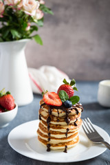 Stack of pancakes with strawberry and chocolate sauce, flowers on dark background. Copy space. Close up, side view