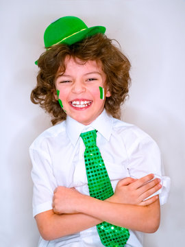 Hispanic child boy having fun during Saint Patrick celebrations over a light background. I am smiling a boy with a green shamrock and Irish flag on my cheek. Patrick's Day celebrations.