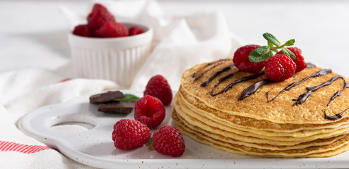 Maslenitsa concept banner. Stack of Russian-style pancakes with raspberries, mint and chocolate sauce. Close up