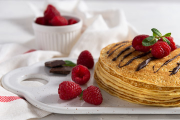 Stack of crepes with berries and chocolate sauce for breakfast on plate, closeup, horizontal, space for text