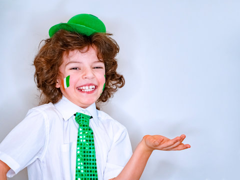 Saint Patrick celebrations over a light background. I am a smiling boy with a Irish flag on my cheek holding an imaginary subject in my hand. Copy space