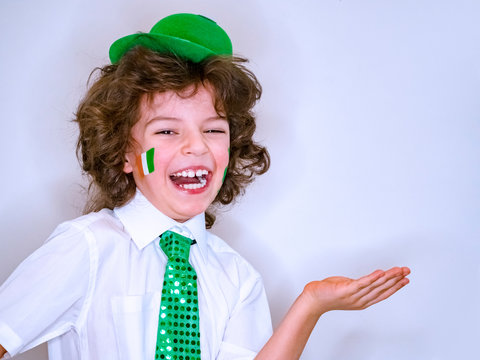 Saint Patrick celebrations over a light background. I am a smiling boy with a Irish flag on my cheek holding an imaginary subject in my hand. Copy space