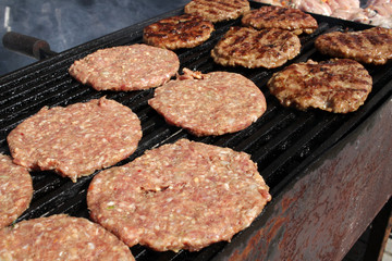Burgers on a grill. Grilled meatballs on a BBQ. Roasted minced meat on a barbecue. Grilled burgers. Fast food on the street. Healthy or unhealthy food concept.
