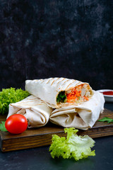 Delicious shawarma sandwich on a black background. Burritos wraps with grilled chicken and vegetables, greens. Fajitas, pita bread. Traditional Middle Eastern appetizer. Healthy food. Mexican cuisine.