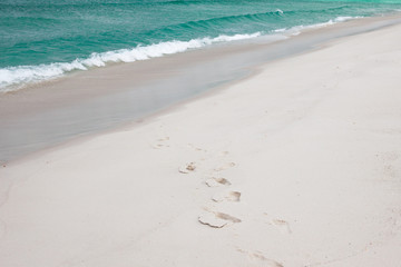 A line of foot prints in the sand mark an otherwise pristine stretch of white sandy beach fringed with crystal clear jade coloured ocean.