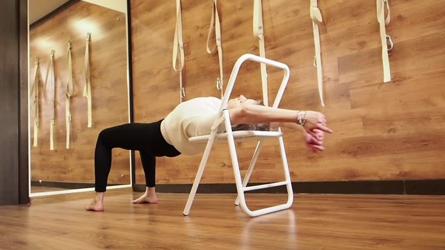 Yoga practitioner doing exercises with a chair that is used as a prop to perform various assan. Flexibility concept. Slow Motion